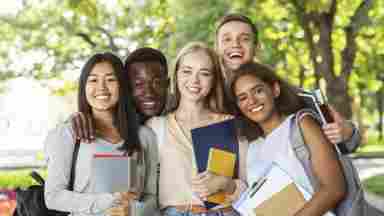 A diverse group of teenage students (college or high school) are holding school books and smiling to the camera.