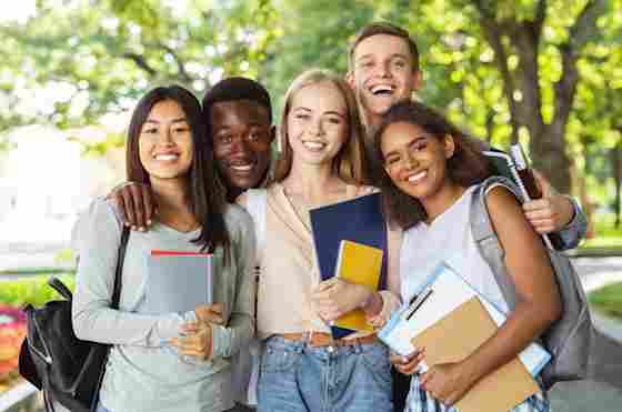 A diverse group of teenage students (college or high school) are holding school books and smiling to the camera.
