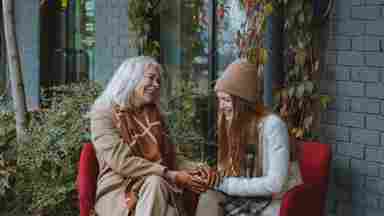 Senior woman talking and smiling with young woman outdoors.