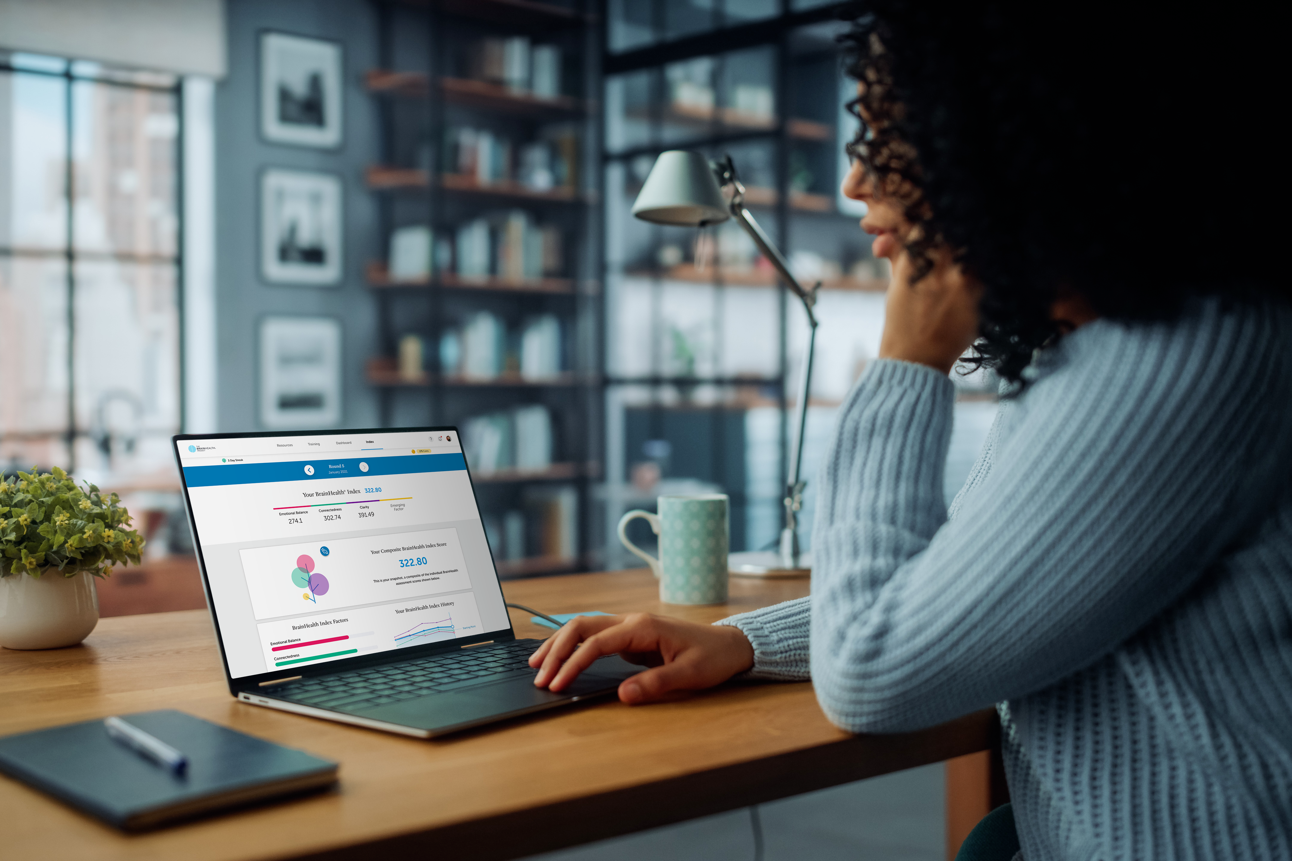 A Black woman wearing a blue sweater sitting at her laptop and checking her BrainHealth Index.