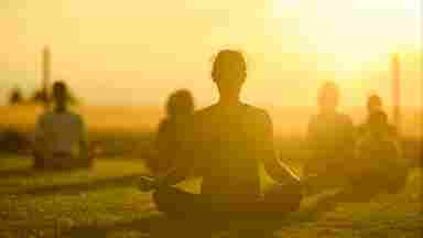 People practicing yoga or meditation outdoors in the orange glow of the sun.