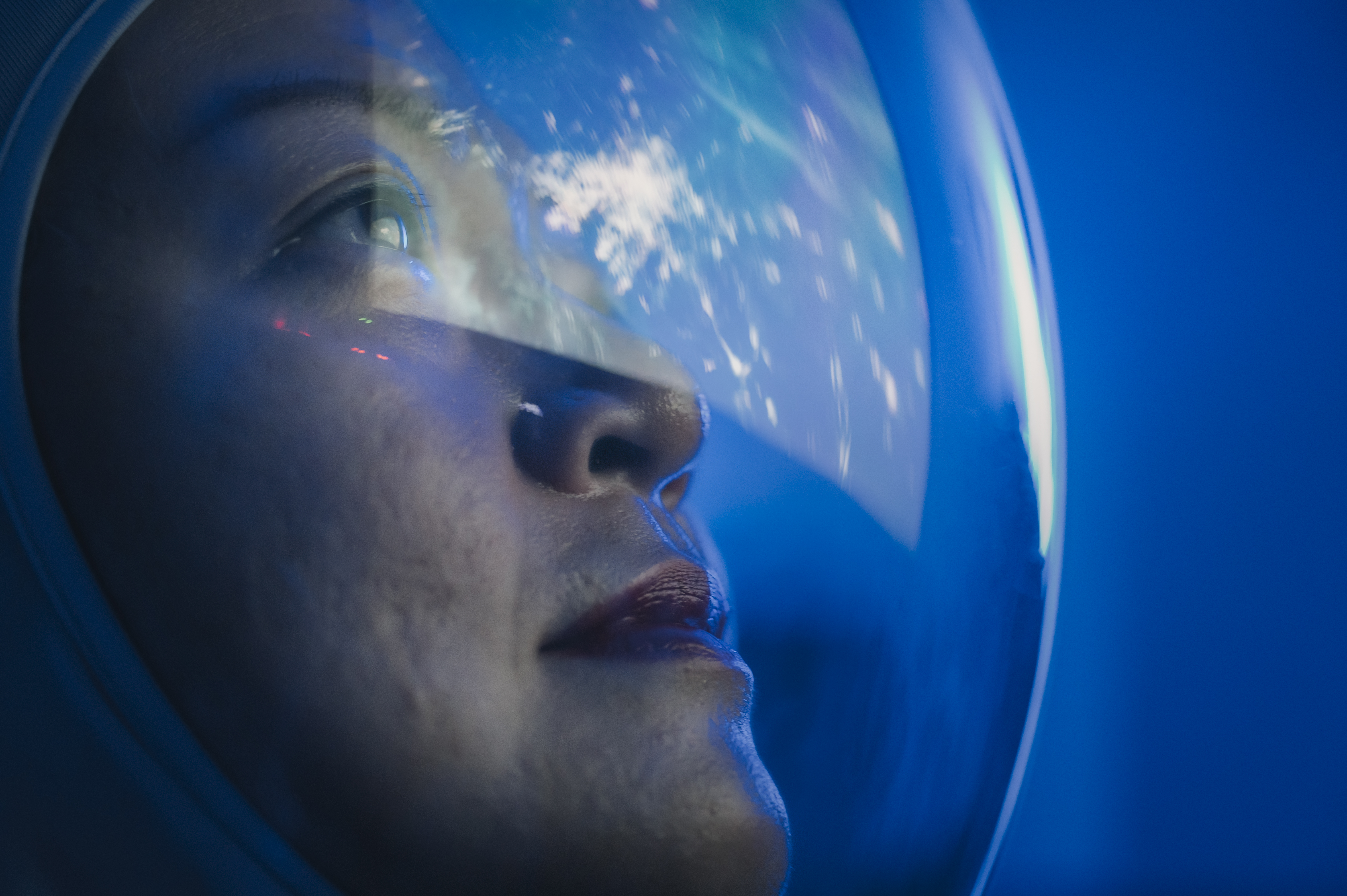 Female Asian astronaut looks at the Earth as its image reflects on her helmet. 