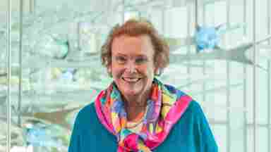 Bonnie Pitman w/ multicolored scarf in front of blue, green lights, landscape. Director Art-Brain Innovations, Center for BrainHealthDistinguished, Scholar in Residence for The Edith O’Donnell Institute of Art History (EODIAH)