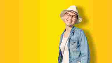 A happy young adult woman bald in hat and casual clothes enjoying life with a yellow background iStock- 1163811833