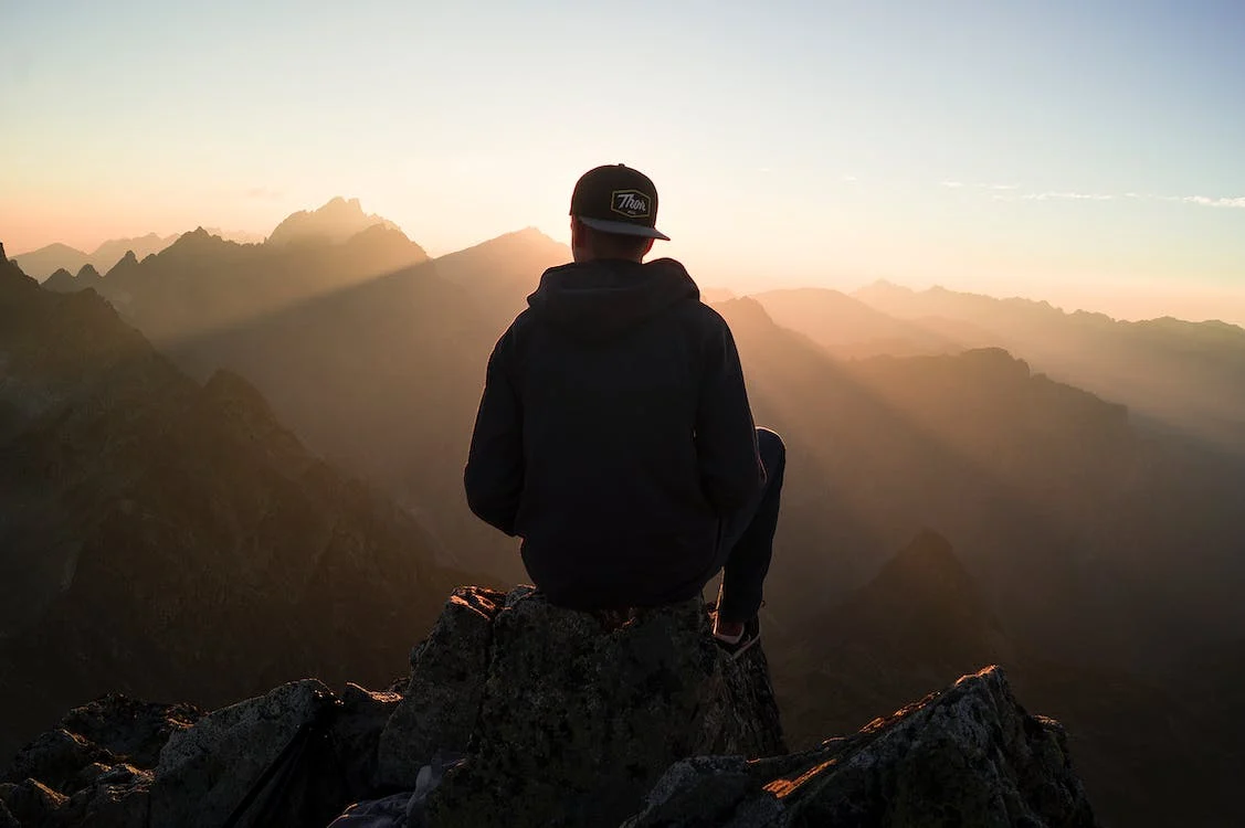 An anonymous man sitting on a mountain edge over looking a sunset.