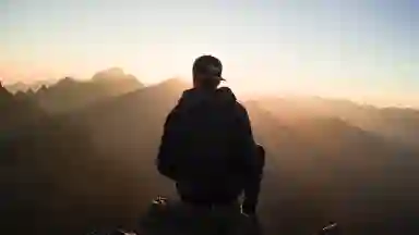 An anonymous man sitting on a mountain edge over looking a sunset.