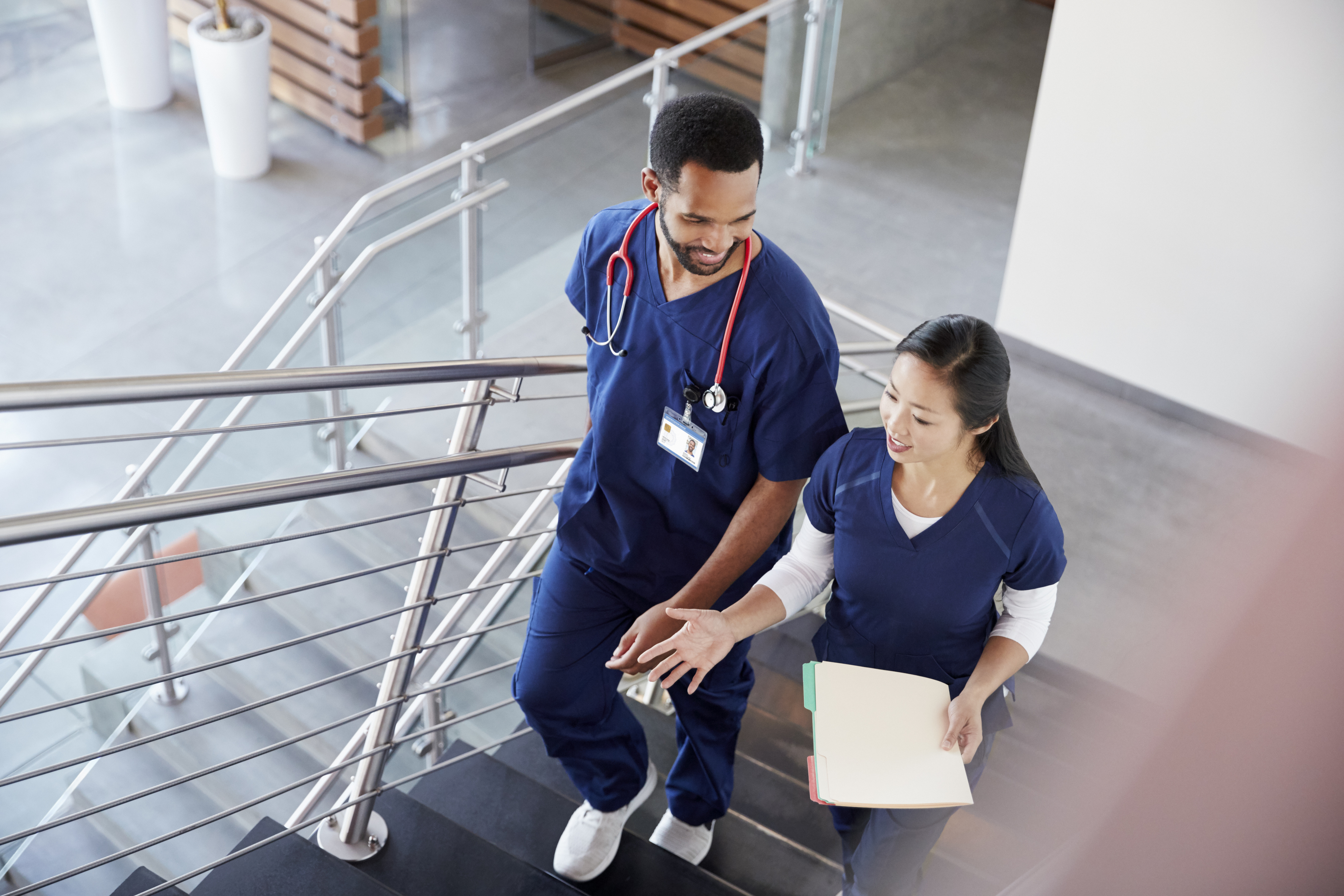 Two healthcare colleagues converse while walking up the stairs in a hospital.