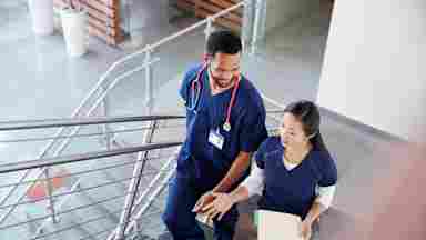 Two healthcare colleagues converse while walking up the stairs in a hospital.