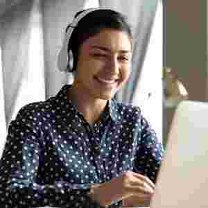 A happy woman is on her laptop while wearing headphones. Used for home page promo.