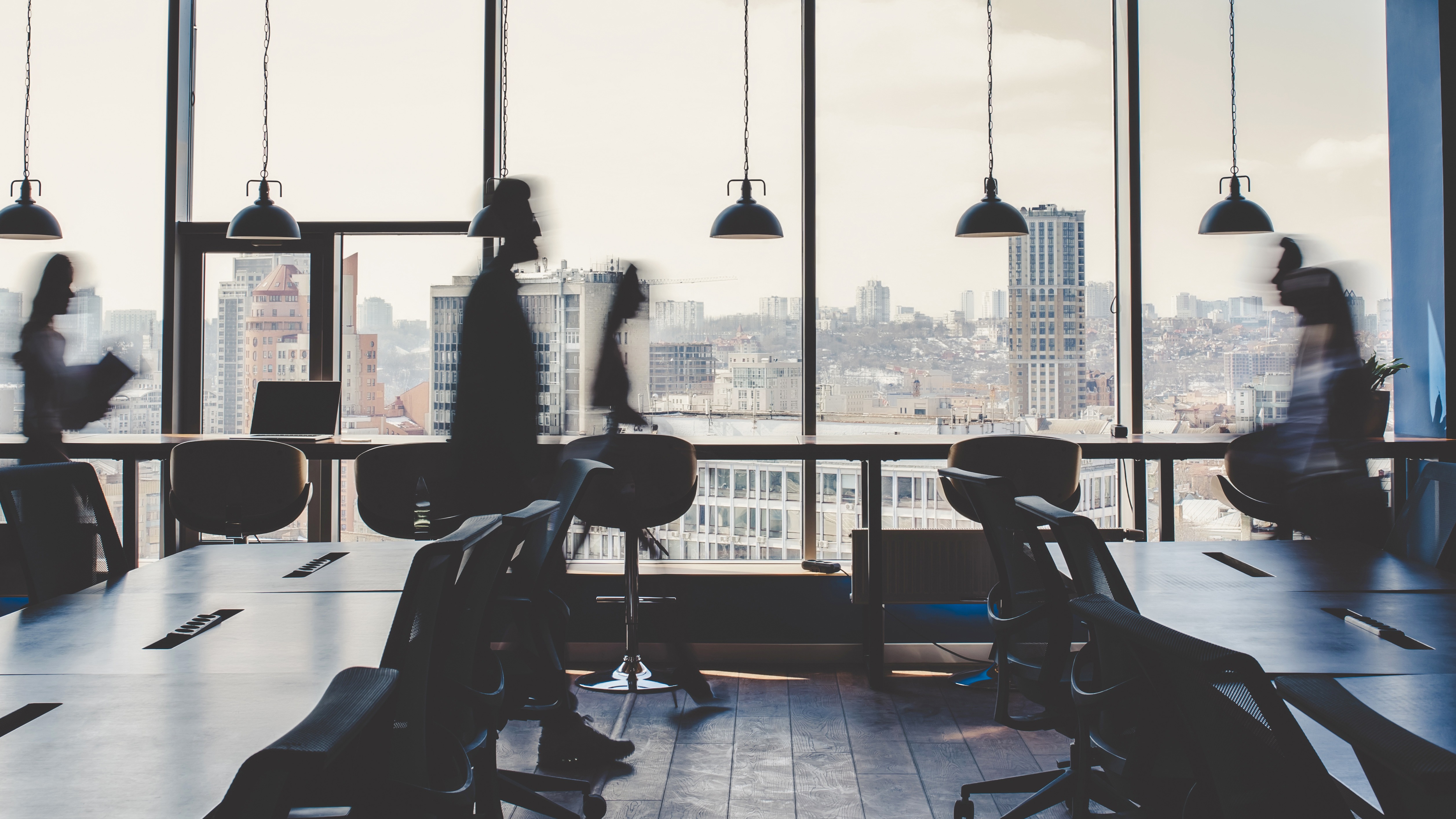 Blurred silhouettes of people moving through a modern office with large windows overlooking a city skyline.