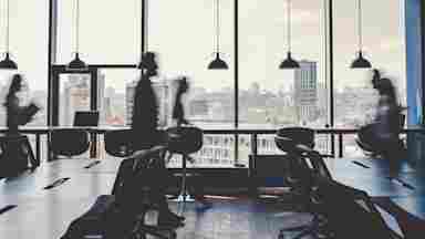 Blurred silhouettes of people moving through a modern office with large windows overlooking a city skyline.