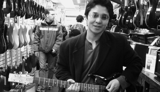 Dr. Yune Lee with sunglasses holding a guitar in a music shop. For "hearing Loss and Cognition" article. 