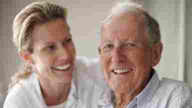 Mature father in his seventies smiling at the camera with his caregiver or daughter.