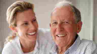 Mature father in his seventies smiling at the camera with his caregiver or daughter.