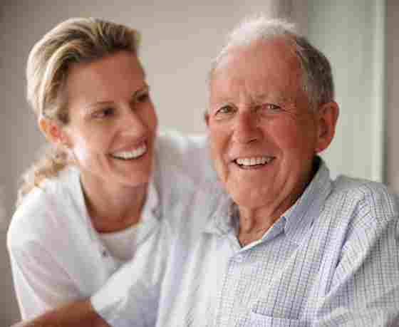 Mature father in his seventies smiling at the camera with his caregiver or daughter.