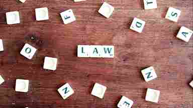 A set of scrabble letters arranged to spell LAW on a dark brown wood table.