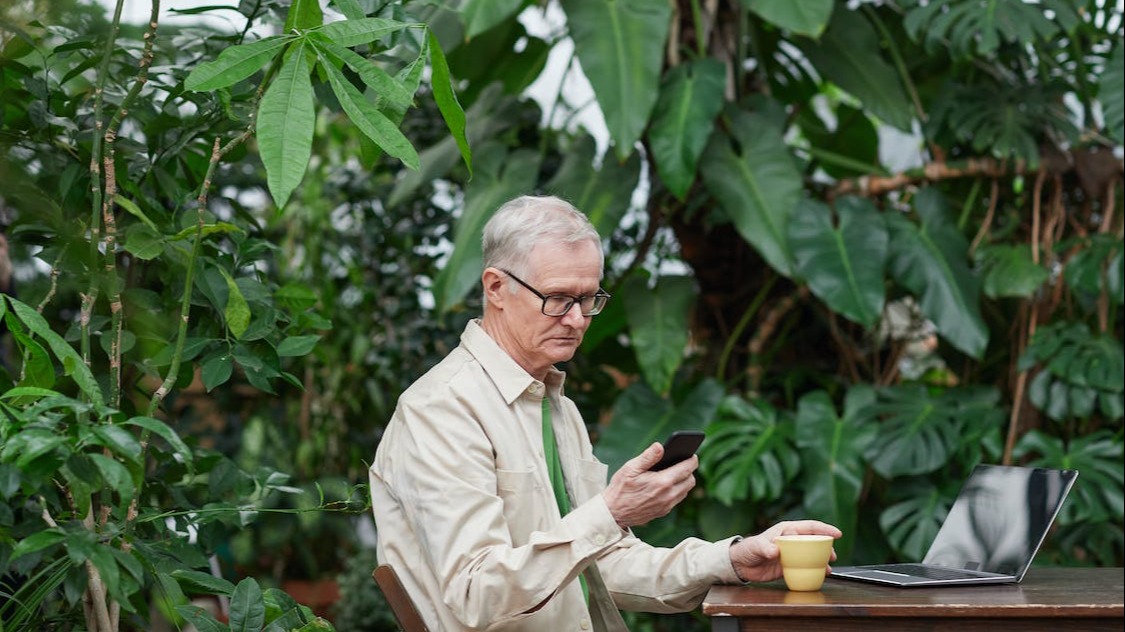 Older man looking at his smart phone surrounded by greenery