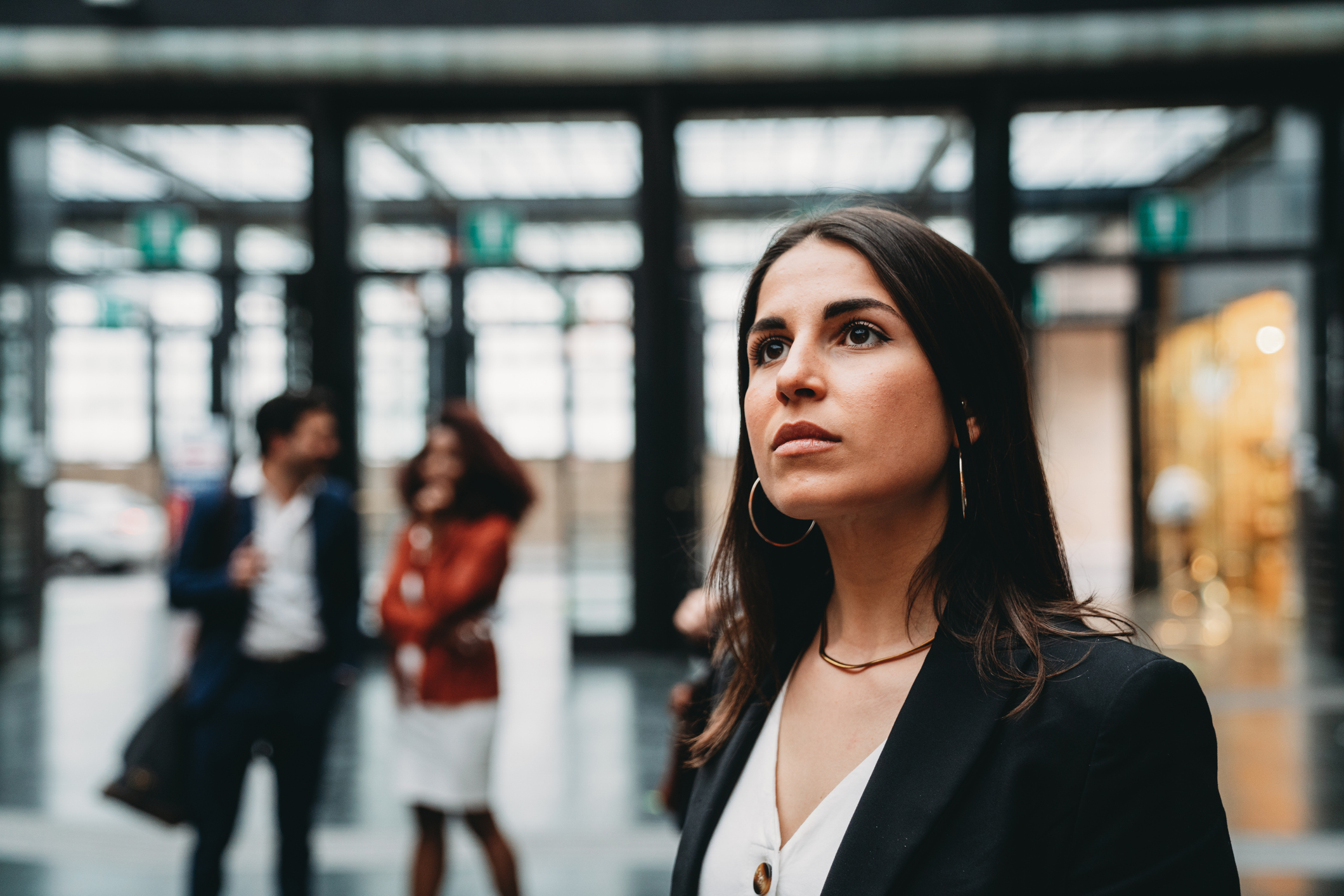 A young professional looks upward with hope as people talk behind her.