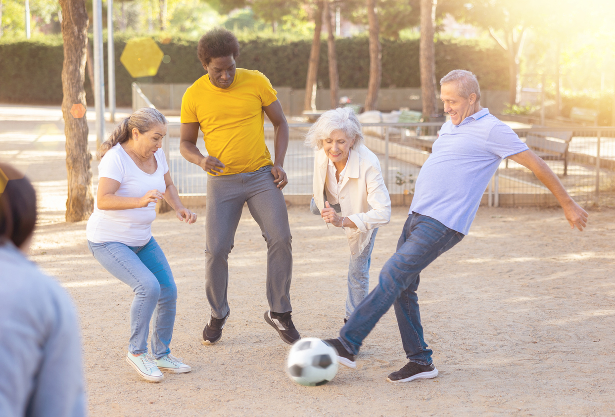 Cheerful group of mixed-race, middle-aged and older adults playing soccer outdoors.