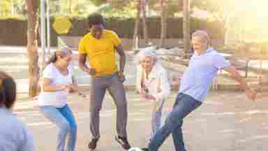 Cheerful group of mixed-race, middle-aged and older adults playing soccer outdoors.