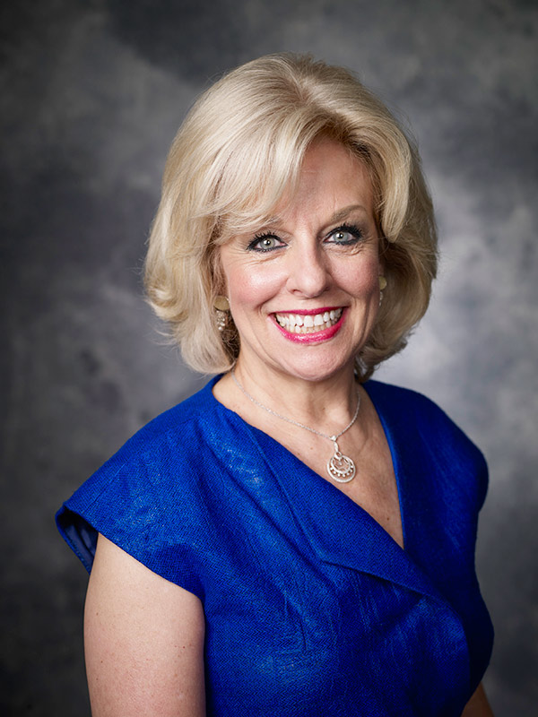 A professional headshot of Dr. Sandra Bond Chapman. She is smiling and wearing a bright blue top against a mottled grey backdrop.