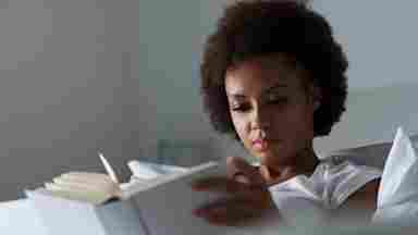 A young person of color reading a book in a peaceful room.