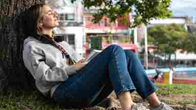 A college student rests under a tree in the community park.