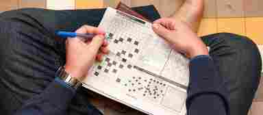 A young person sits cross-legged on the floor working on a crossword puzzle.