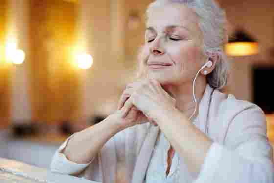 A mature woman with earphones listens to music with a serene expression on her face.
