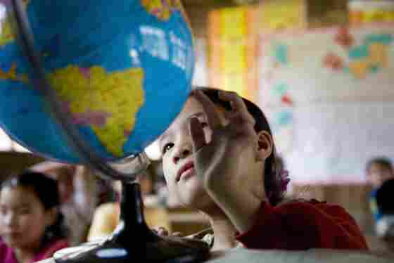 A child sitting in a classroom observing a spinning globe.