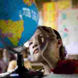 A child sitting in a classroom observing a spinning globe.