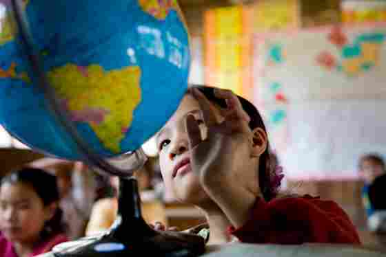 A child sitting in a classroom observing a spinning globe. For limitless campaign.