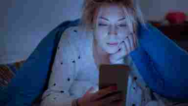 Teenage girl laying in bed reading text messages on her phone at night.