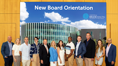 A group of eleven new board members posing in front of a Center for BrainHealth New Board Orientation banner.
