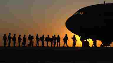 A silhouette of soldiers getting on a plane at sunset.