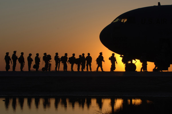 A silhouette of soldiers getting on a plane at sunset. 