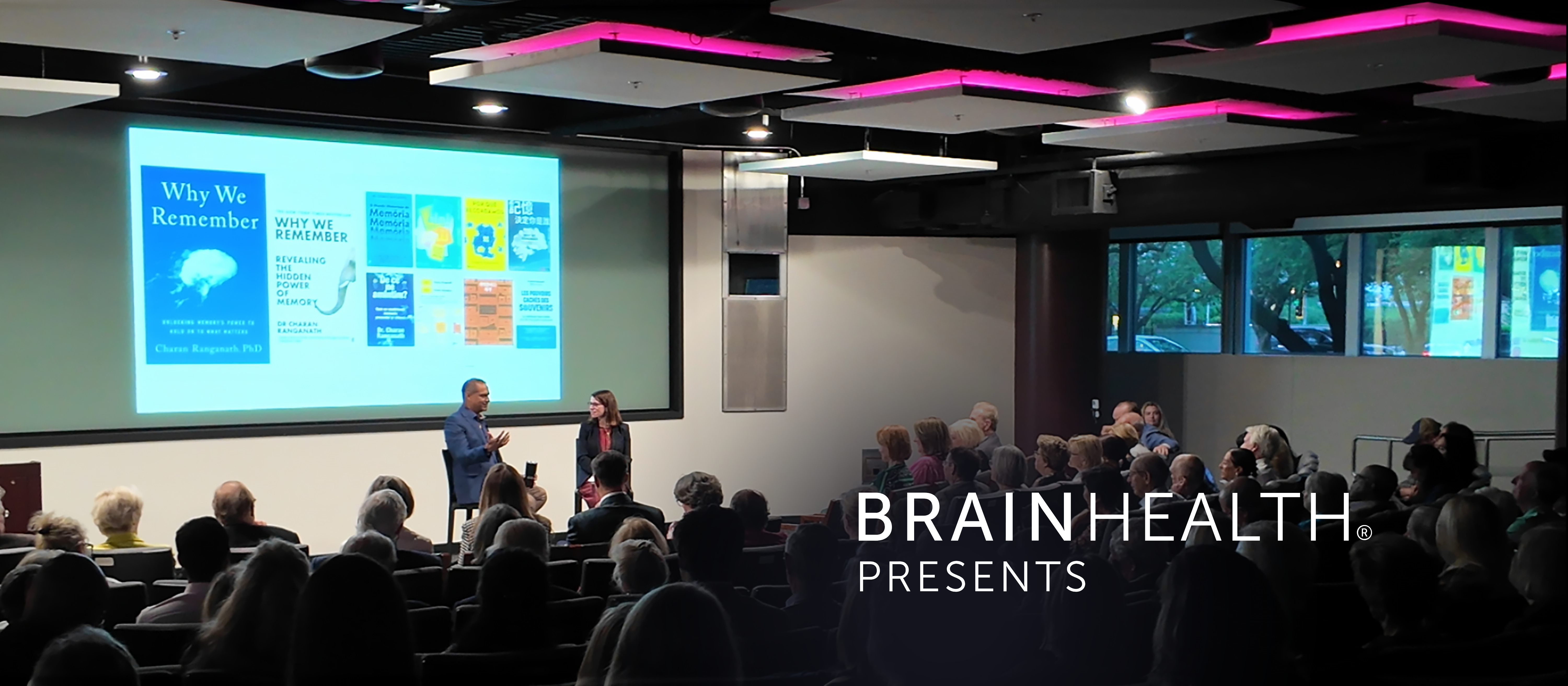 Photograph of neuroscientist Charan Ranganath, PhD, engaged in a fireside chat with Jennifer Zientz during the BrainHealth Presents speaker series, pictured in a crowded auditorium with modern lighting and projected image of publications and media by Dr. Ranganath.