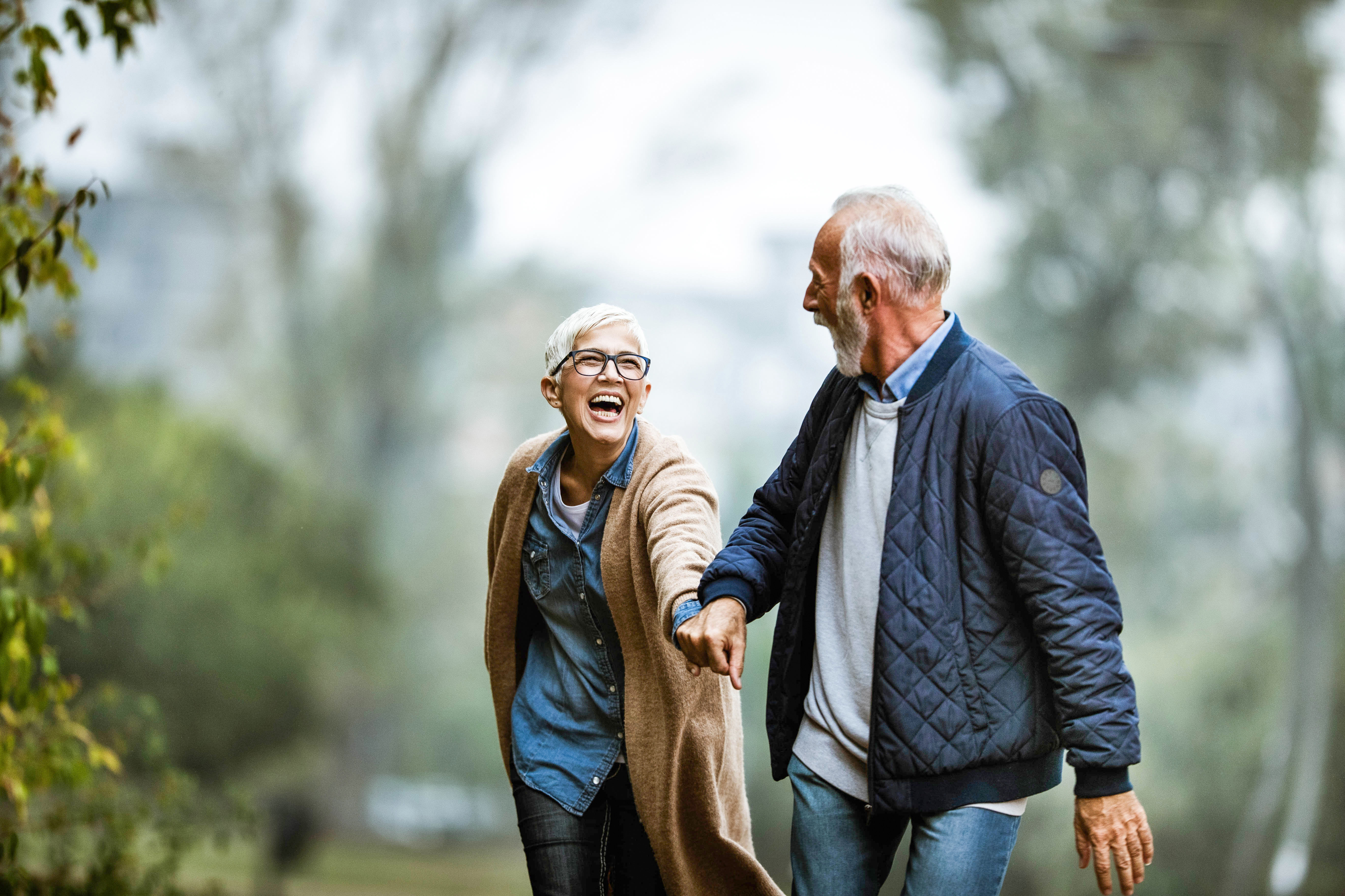 A smiling, happy senior couple walk hand-in-hand in a park together.