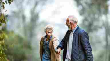 A smiling, happy senior couple walk hand-in-hand in a park together.