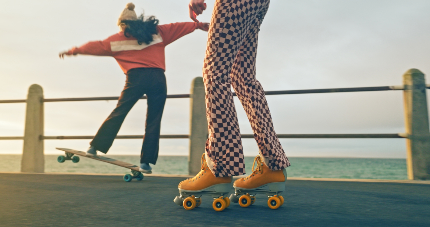Friends skateboard and roller-skate on the boardwalk by the ocean.