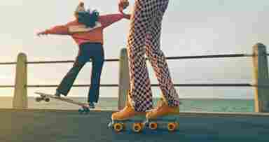 Friends skateboard and roller-skate on the boardwalk by the ocean.