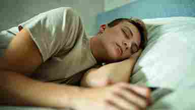 Tired teenager sleeping with their phone beside them.