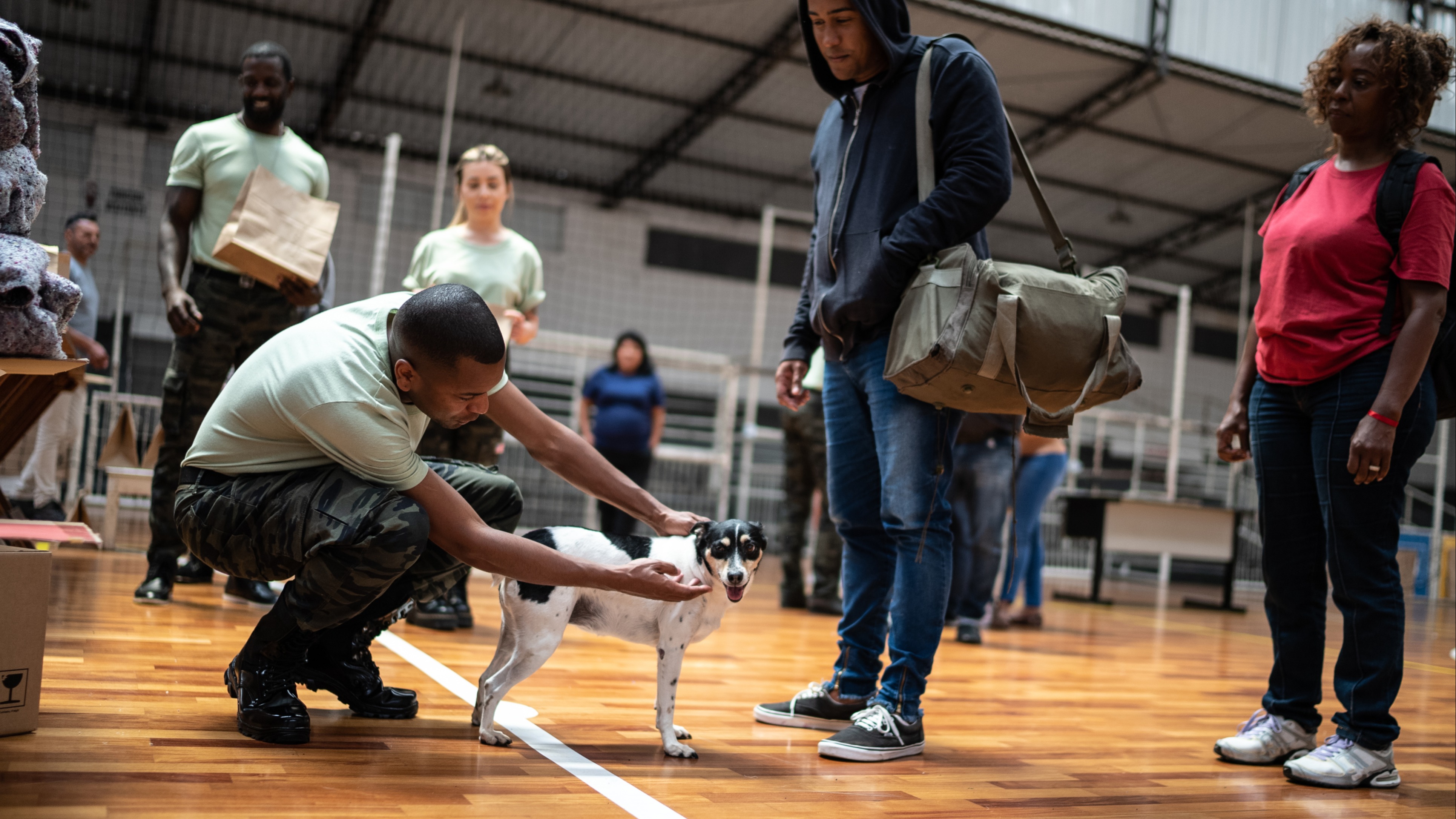 A young soldier comforts a family's dog as they take shelter at a community center after a natural disaster.