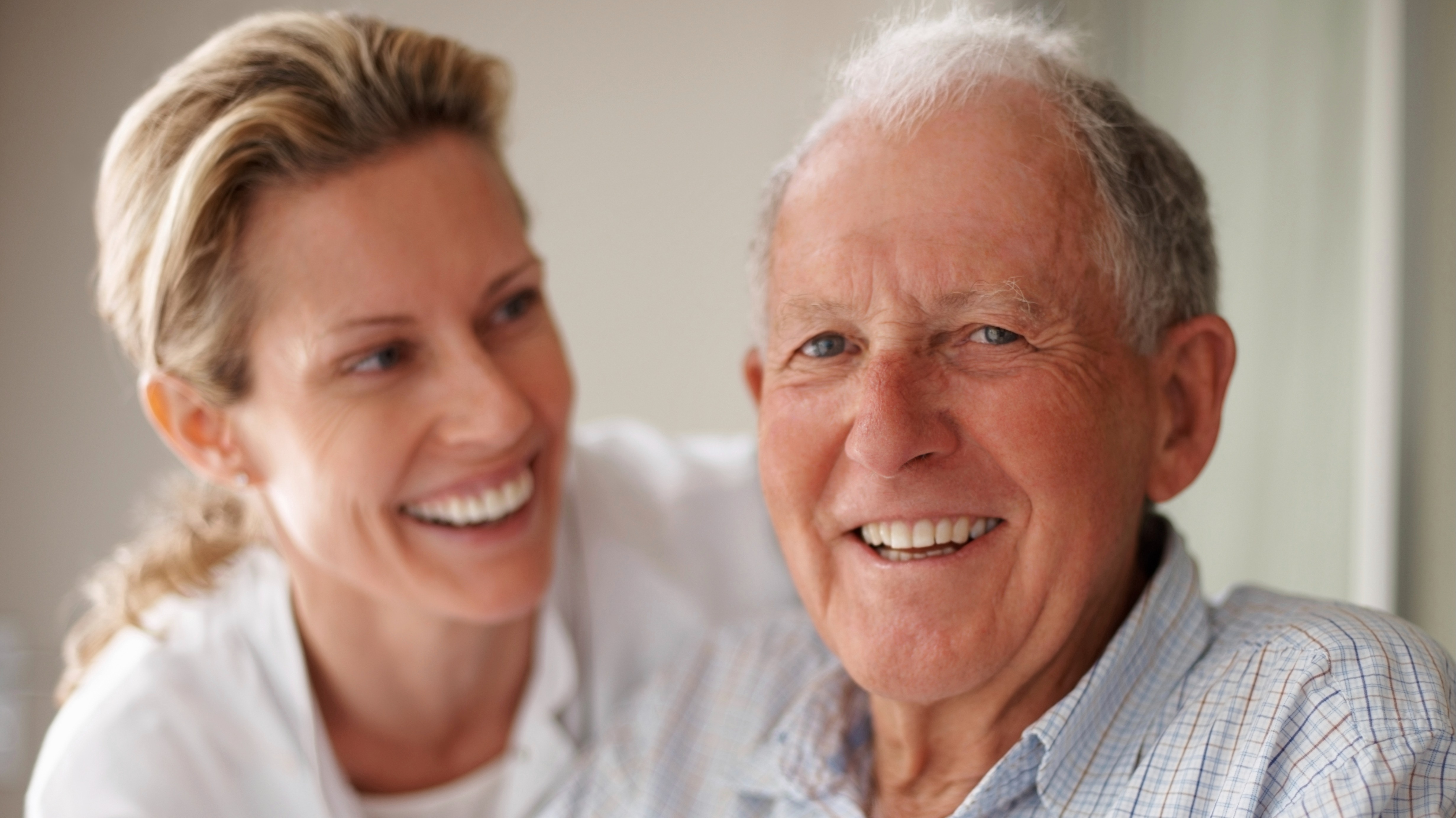 Mature father in his seventies smiling at the camera with his caregiver or daughter.