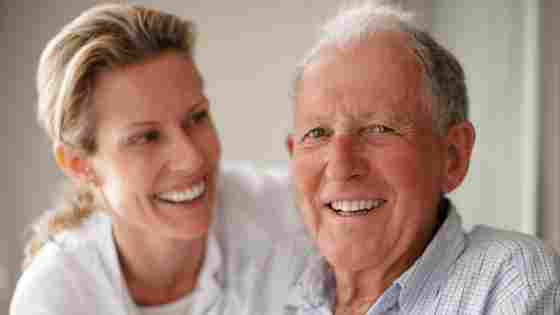 Mature father in his seventies smiling at the camera with his caregiver or daughter.