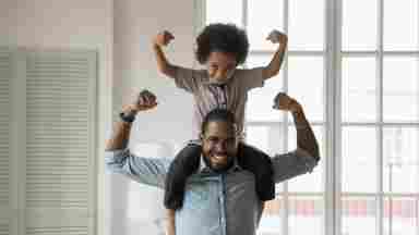 A young son is on his father's shoulders while they both show their biceps.