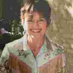 Nancy Wilbur headshot for the board webpage; she is outdoors and wearing a patterned blouse with tassels. She smiles cheerfully at the camera.