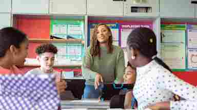 A Black female teacher answers questions and engages with students working in class.