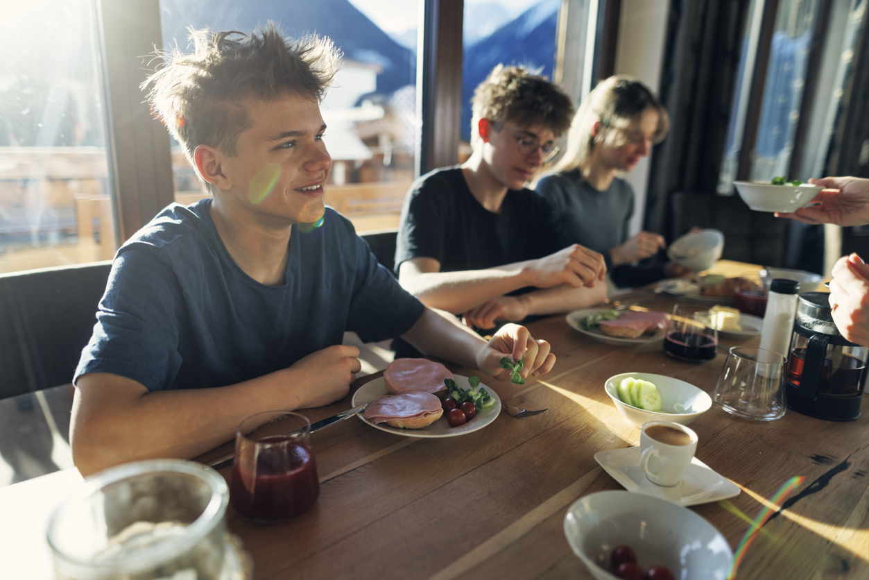 Teenagers eating a healthy breakfast together, with tea, cheese, fruit and vegetables.