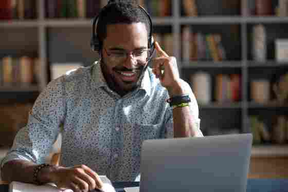 A happy man is wearing a headset on his computer. 